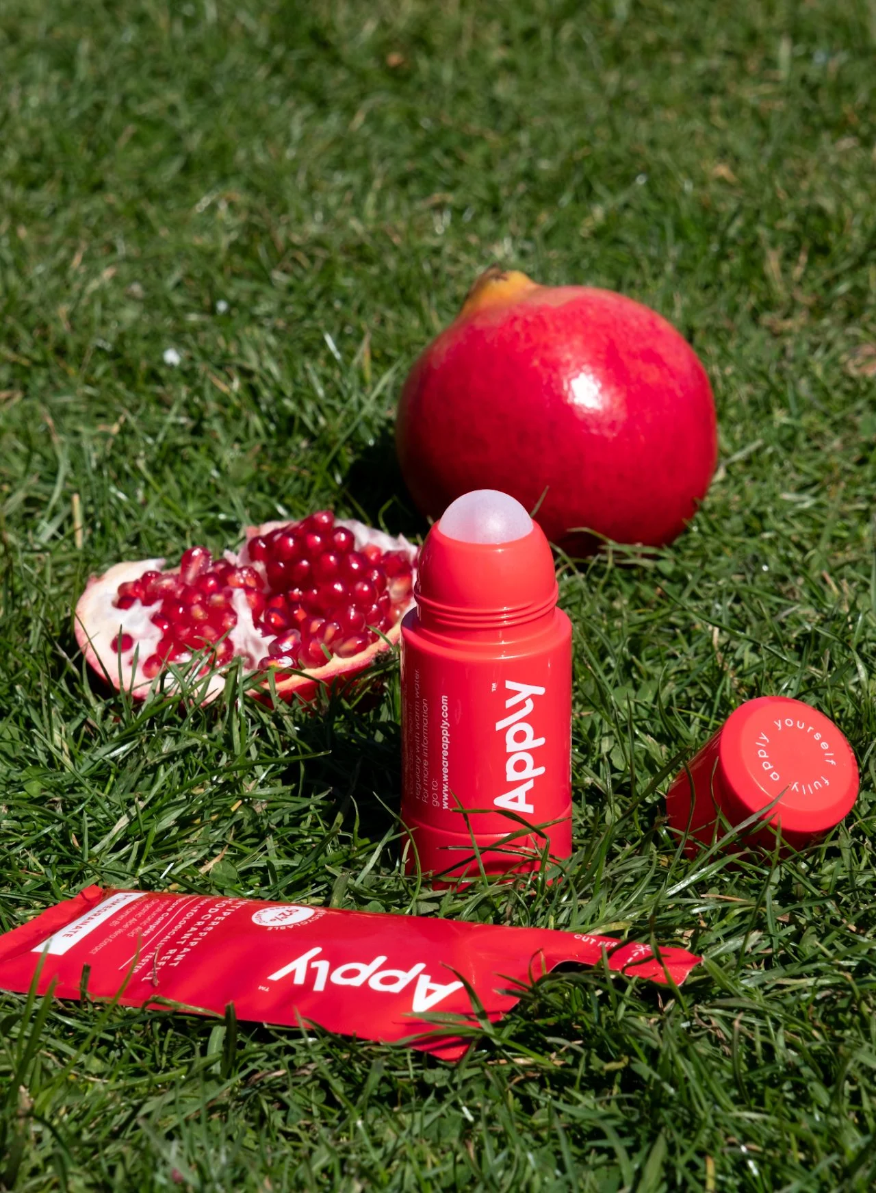Apply's pomegranate roll-on and refill pouch on the grass beside a cut pomegranate