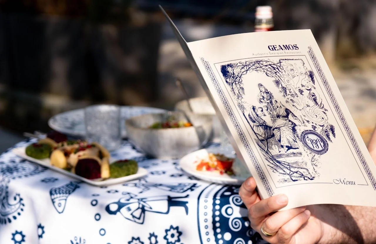 A guest reads the Geamos menu at an outdoor table laid with Georgian dishes