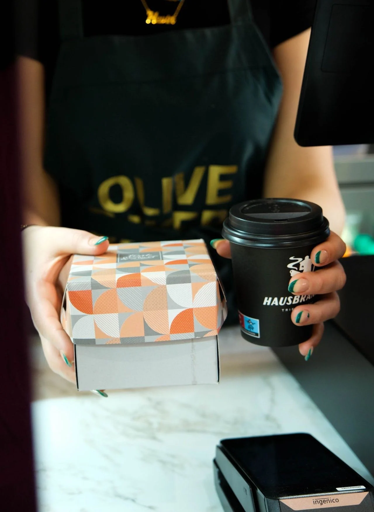 A barista hands over a pastry box and a takeaway coffee