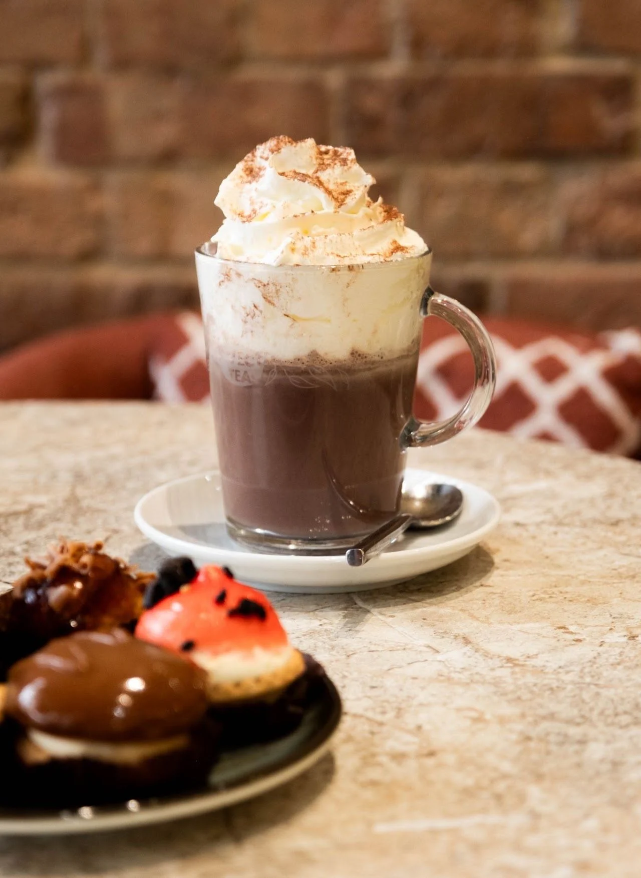 A hot chocolate topped with cream beside cakes