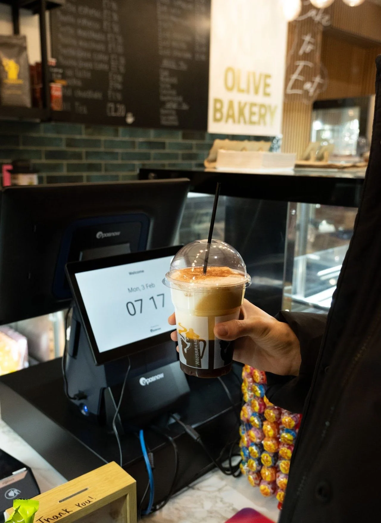 An iced coffee held up at the till at The Olive Bakery